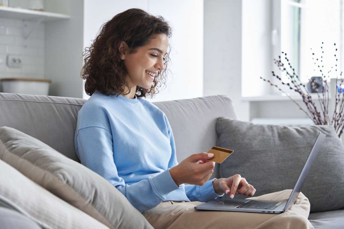 Happy young Hispanic female customer of direct sales holds credit card to place an order